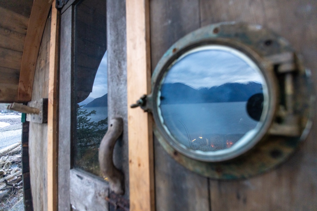 Brass porthole on the sauna door reflecting mountains and the ocean